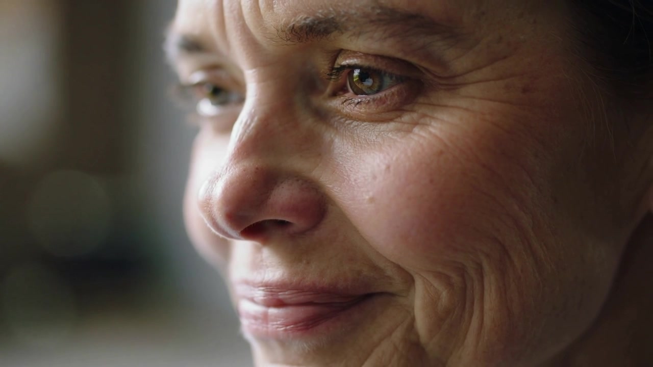 Noticing window light, smiling middle-aged woman softening expression at home, with moist eyes
