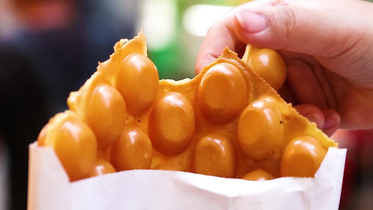 A detailed view of hands holding a bubble waffle in a paper bag, showcasing its texture.