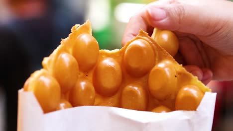 a detailed view of hands holding a bubble waffle in a paper bag, showcasing its texture.
