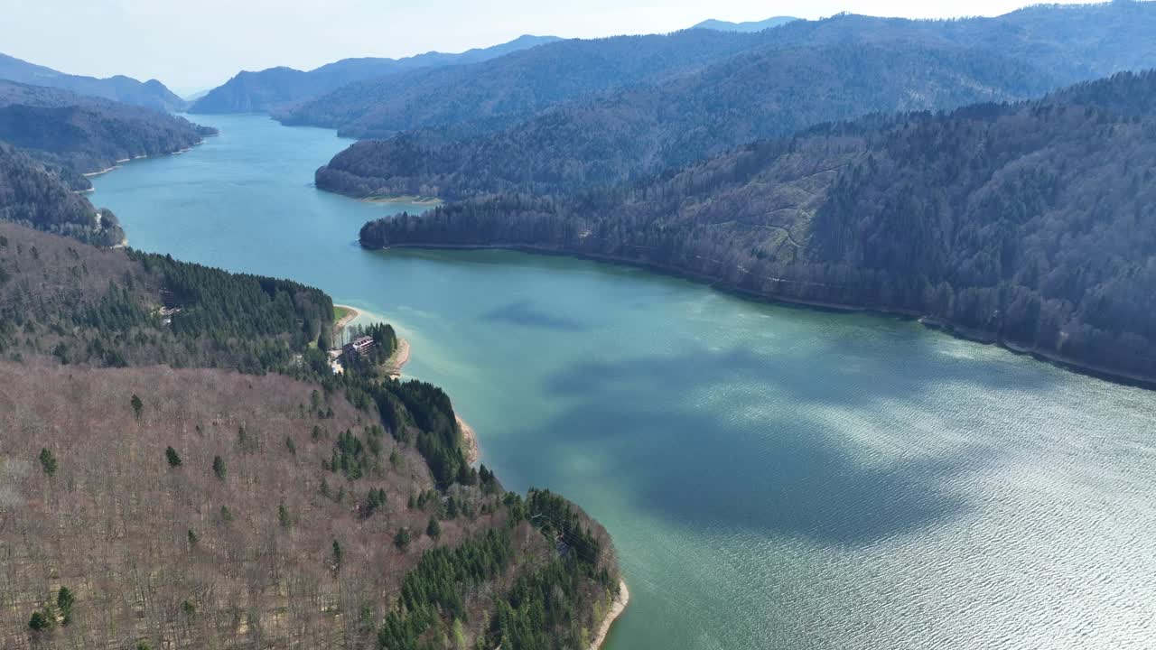 A peaceful blue lake surrounded by forests and mountains in a serene setting, aerial view