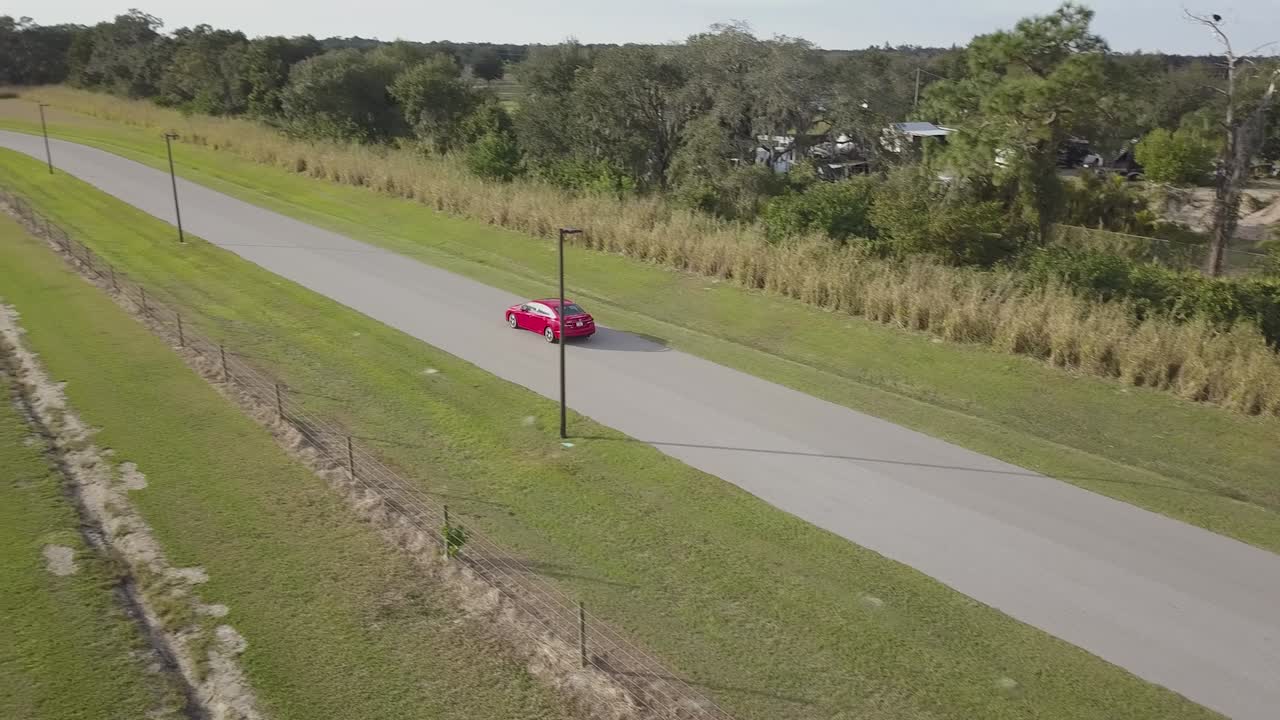 Aerial View of Red Sports Car Driving Away on Empty Country Road at Sunset
