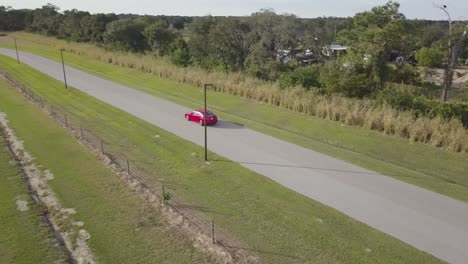 aerial view of red sports car driving away on empty country road at sunset