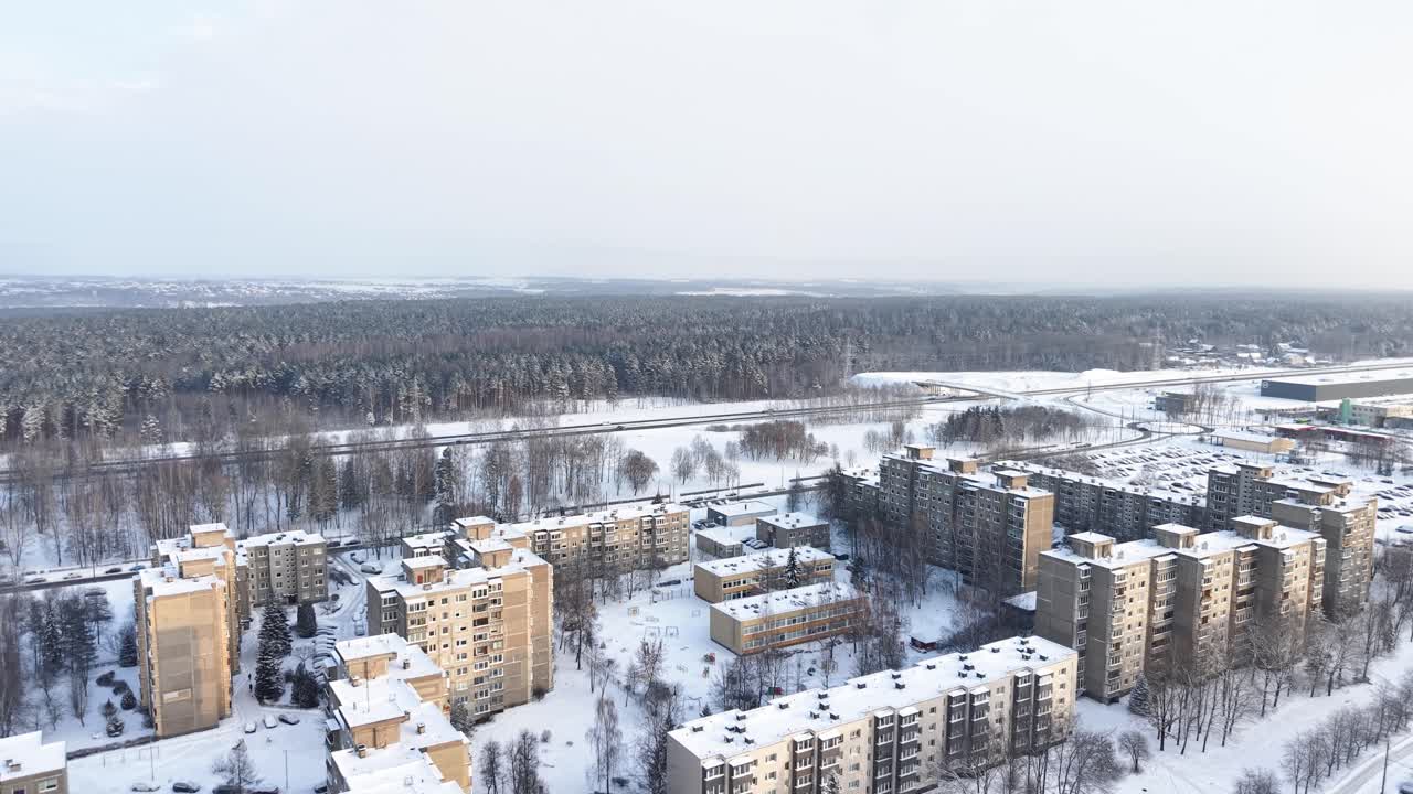 Ein atemberaubendes Drohnenvideo, das ein schneebedecktes Stadtgebiet umgeben von dichten Wäldern einfängt. Die klare Winterszene bietet einen ruhigen Überblick über Wohngebäude unter einem blassen Himmel.