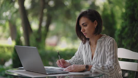 pensive woman brunette arabic hispanic ethnic group sits at a table in a summer cafe with a laptop. serious business woman pondering problem solving and business development strategy