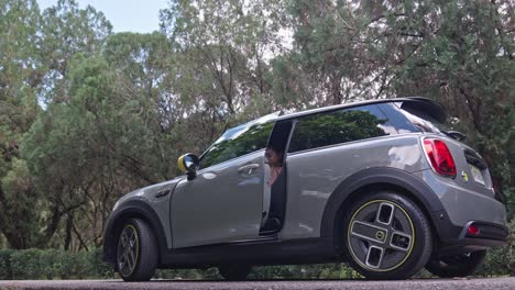 atractiva joven rubia deportiva con polainas abre la puerta del coche eléctrico mini cooper gris para entrar y sentarse en el asiento del conductor