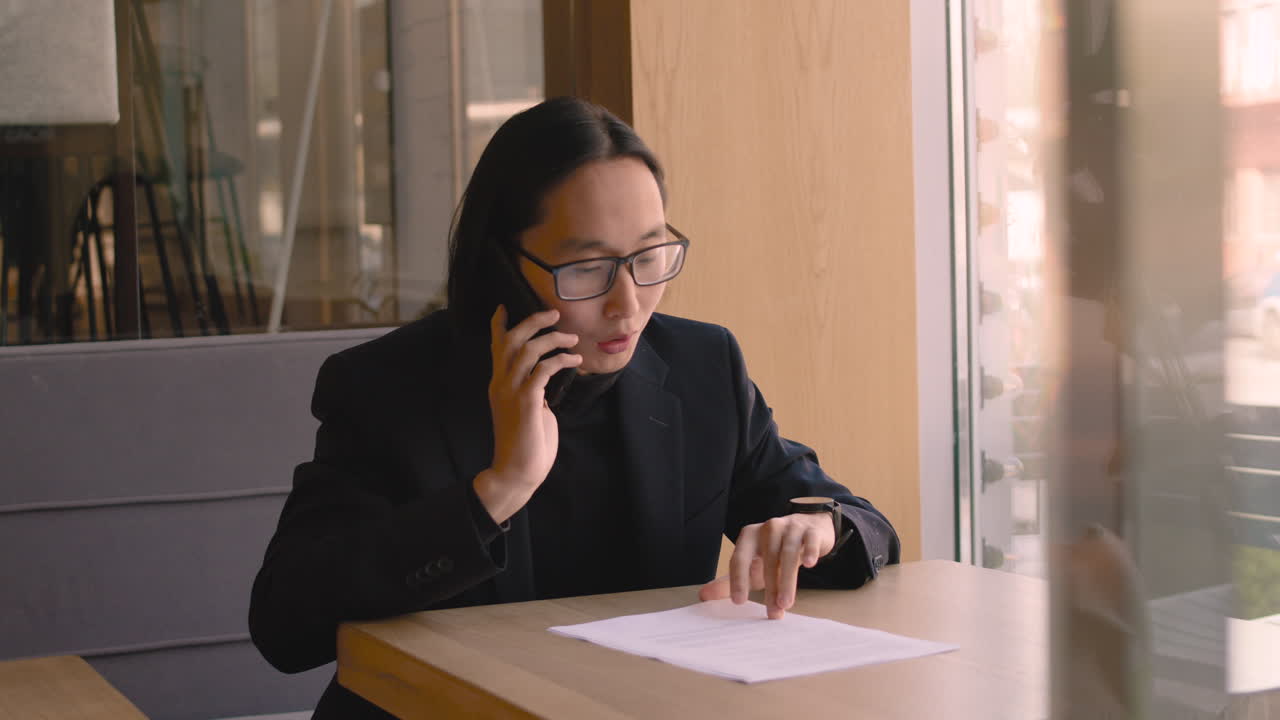 진지한 사업가가 휴대폰으로 수다를 떨고 커피숍에서 종이 문서를 보고 있다