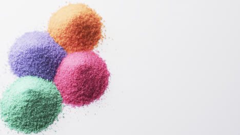 video of close up of heaps of multi coloured sand grains and copy space on white background