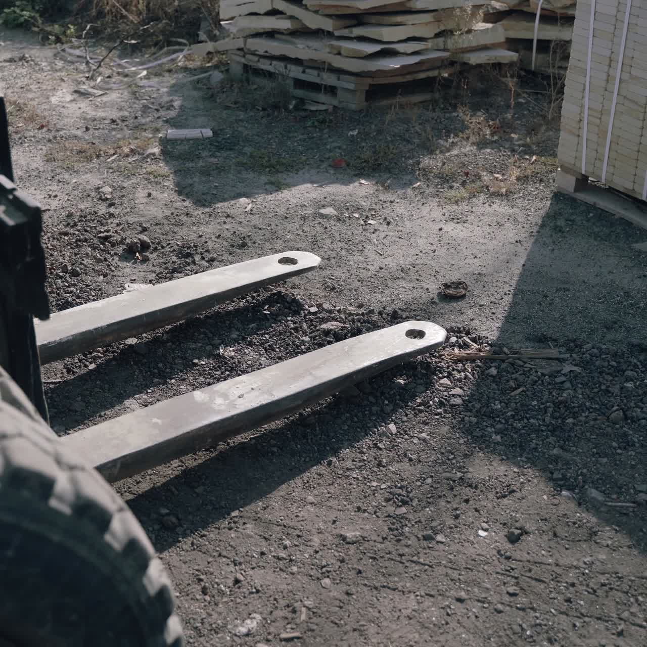 a forklift is approaching the pallet with bricks and lifting it to moving to another place in the street.