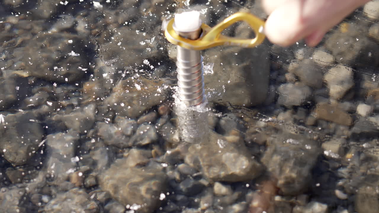 Medium shot and clear look of an ice screw being screwed into a frozen lake.