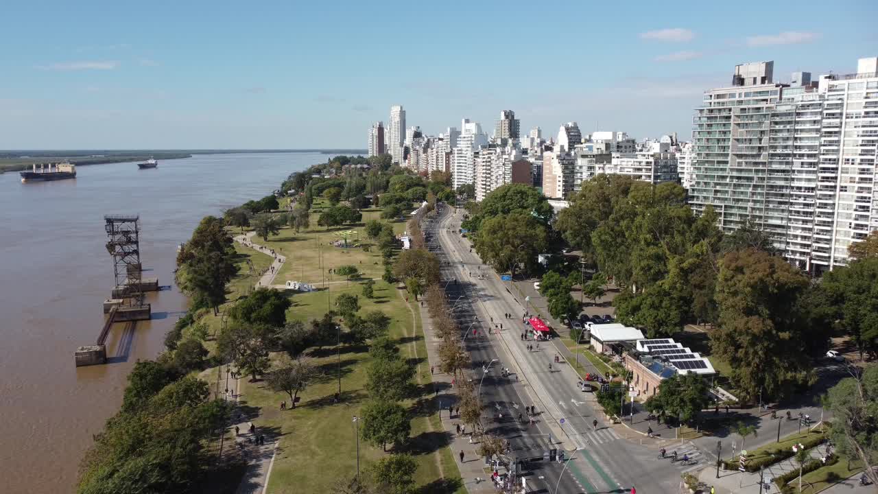 Aerial drone view of the Paraná River, Rosario’s tall buildings, and people strolling along the riverside