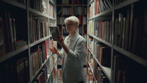 joven seleccionando un libro en el pasillo de la biblioteca débilmente iluminado
