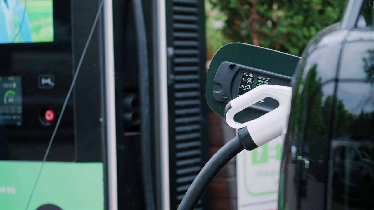 Modern bir istasyonda şarj olan elektrikli araç, araca takılı konektörün yakın çekimiyle.