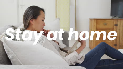 animation of stay at home text over asian woman using tablet at home