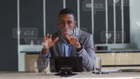 Animation-of-social-media-icons-over-african-american-businessman-having-a-videocall-at-office