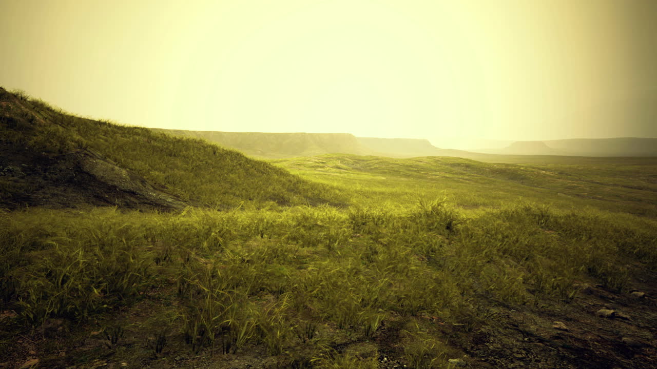 Sunrise illuminating grassy hills with distant mountains in soft focus