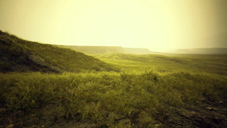 sunrise illuminating grassy hills with distant mountains in soft focus