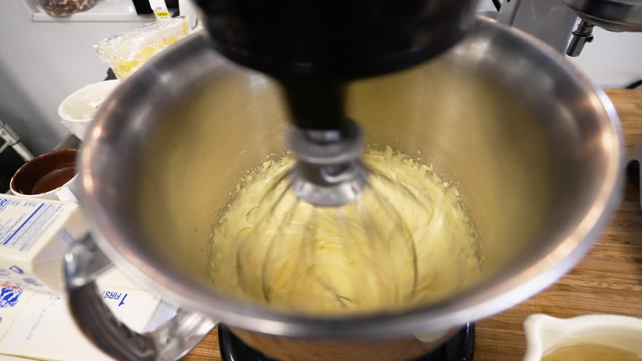 Stainless steel kitchen stand mixer creams butter in stainless handled bowl, slow motion 4K