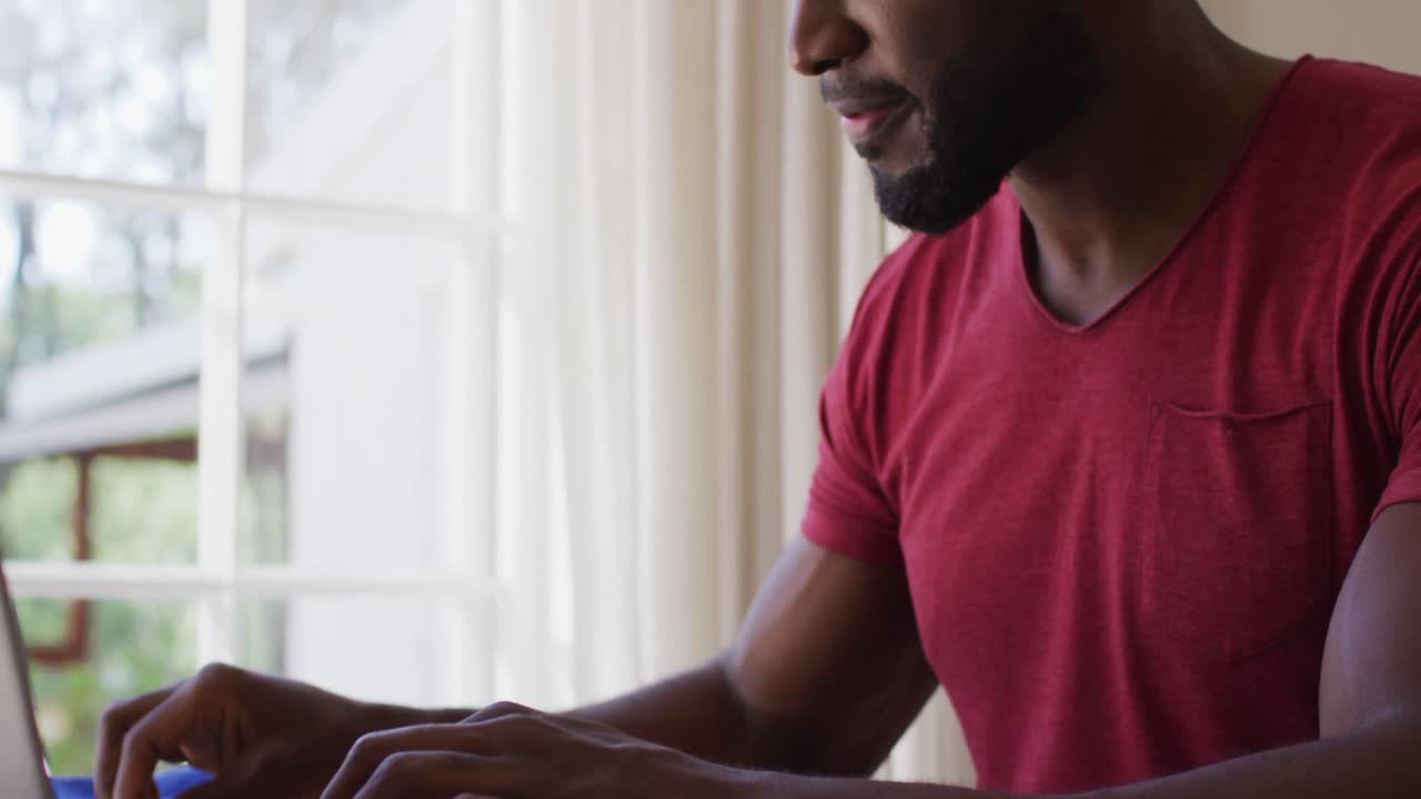 African american man holding pen using using laptop while sitting on his desk at home