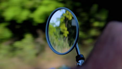 bokeh shot of a man driving a car with the woodlands reflecting in the small mirror