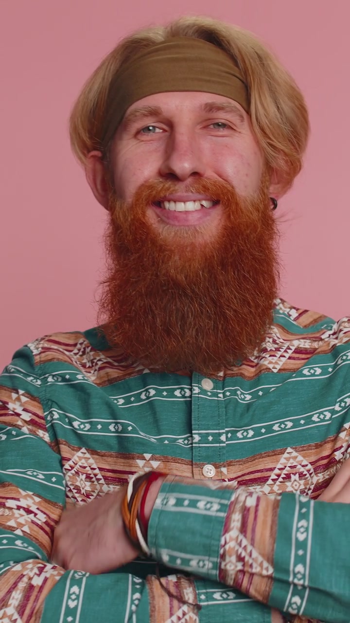 Iloinen parrakas hippi-hipster punapää mies muotimalli kuviollisessa paidassa hymyilee katsoen kameraan.