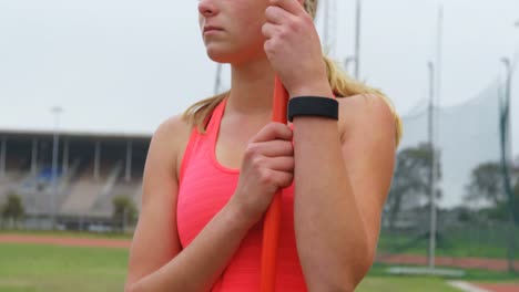 vista frontal de una joven atleta caucásica de pie con un palo de jabalina en un lugar deportivo 4k
