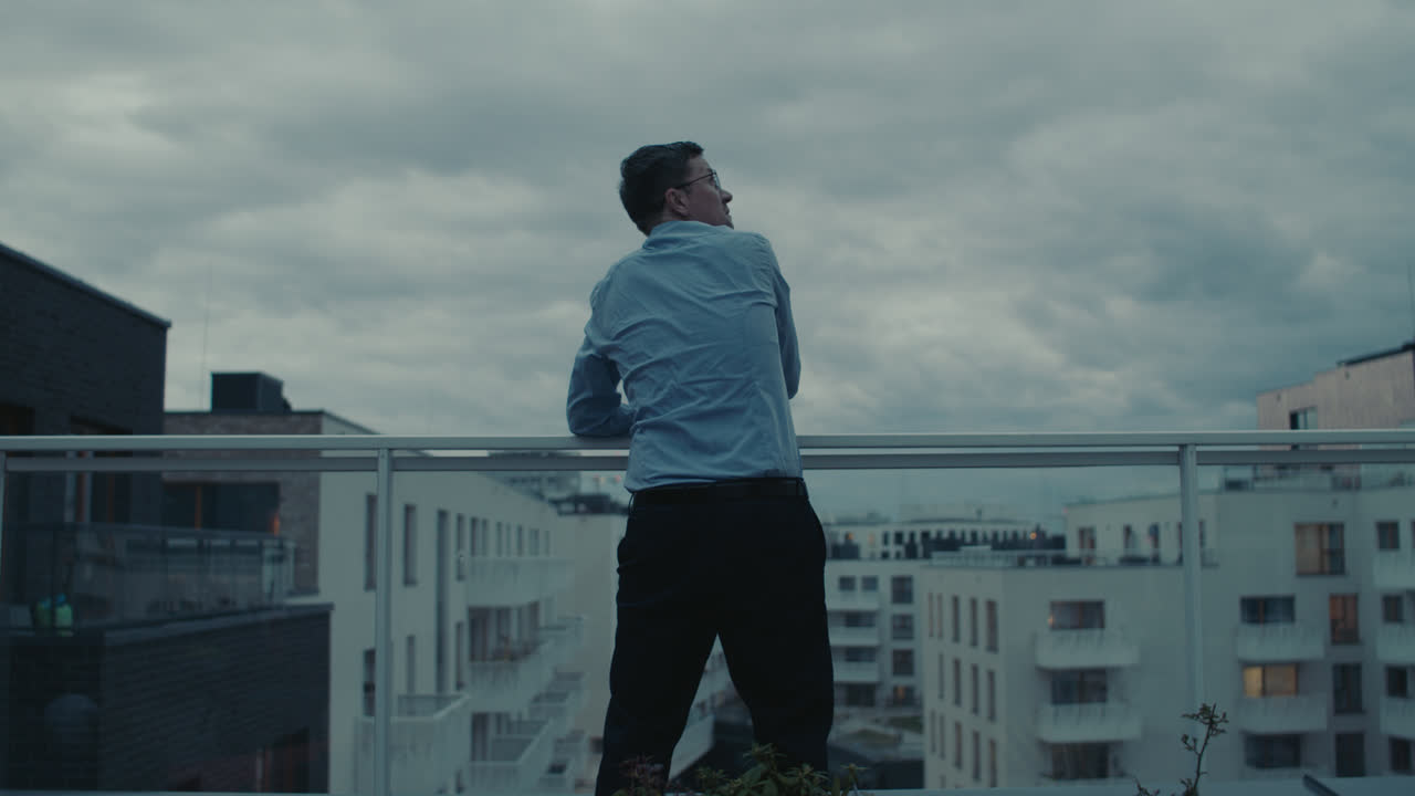 A sad man in a shirt smokes a cigarette on the balcony