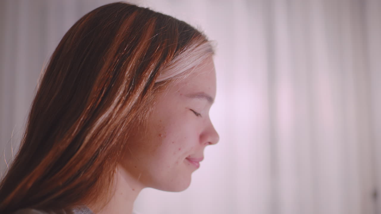 Close side view of young woman with long hair taking tea in soft daylight setting, eyes closed, serene mood, delicate facial expression, highlighting calm atmosphere