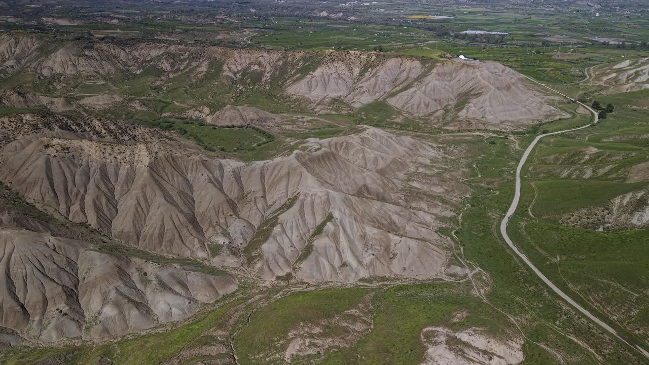 Winding paths through eroded calanchi and grassy patches, aerial establishing tracking left, Calanchi del Cannizzola Sicily Italy