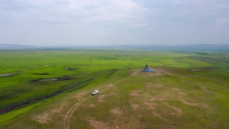 Drone-pulls-away-as-car-drives-down-single-track-dirt-road-on-grassy-hillside,-mongolia