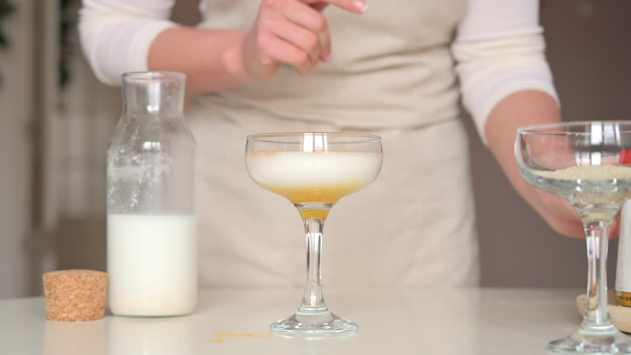 Donna con un grembiule che versa polvere gialla nel latte in un bicchiere da cocktail in cucina