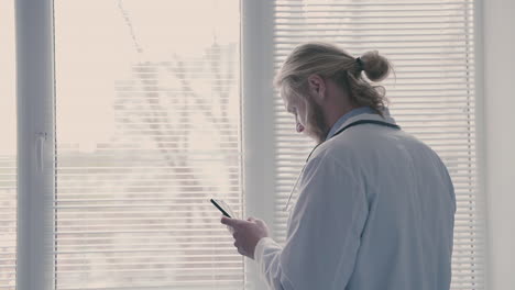 un joven médico con cabello largo y rubio hace una llamada de teléfono móvil