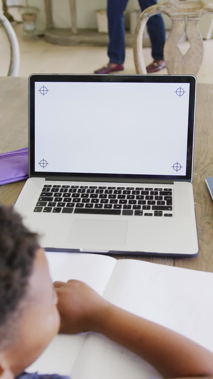 Vertical video of happy african american boy using laptop with copy space, in slow motion
