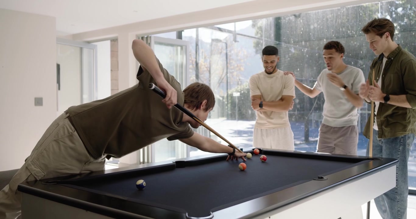 Male friends celebrating successful shot, lining cues and taking shots at home pool