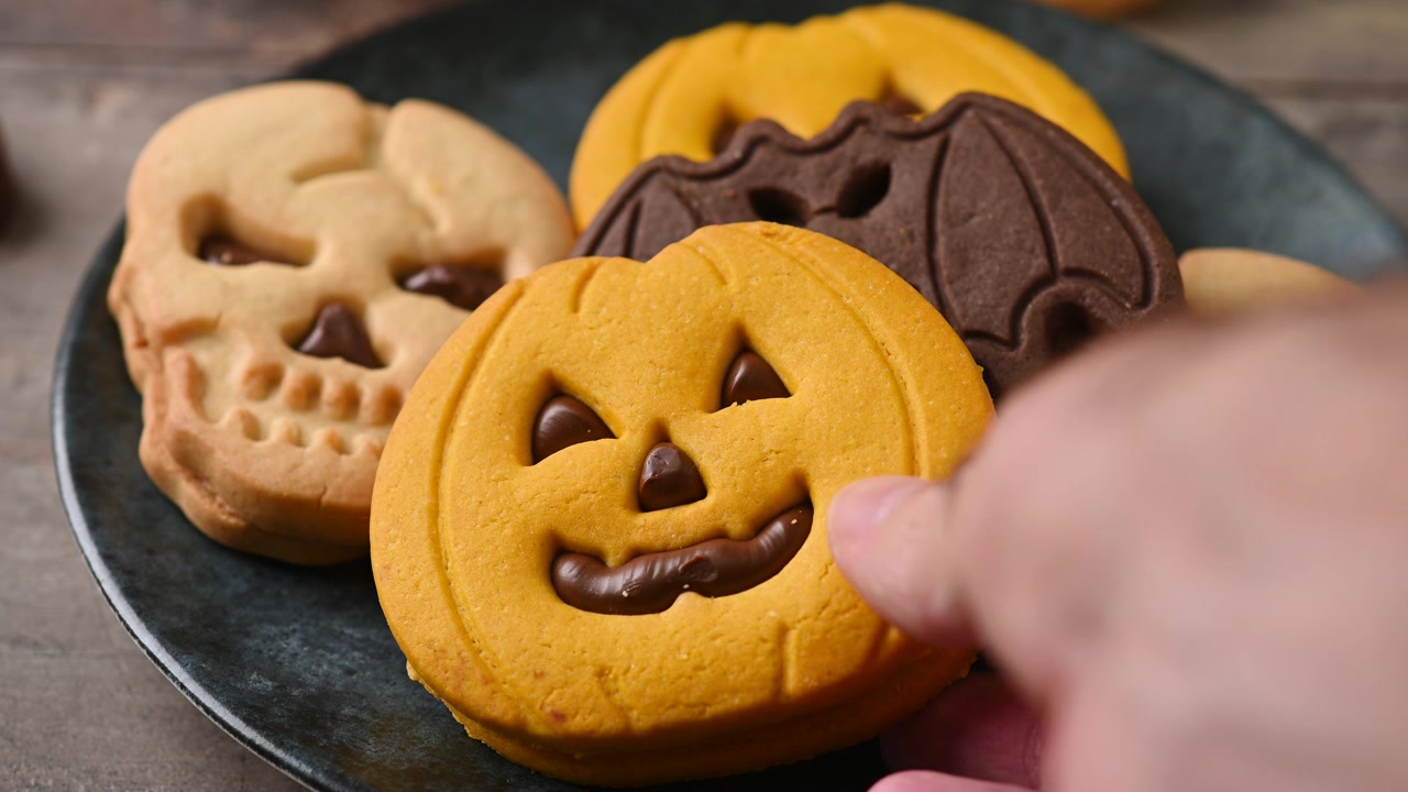 Hand taking a Halloween cookie from a festive dessert plate