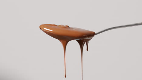 close up of melted chocolate dripping from overflowing spoon against white background with copy space