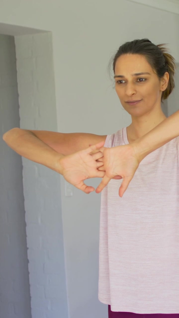 Video vertical: Mujer con camiseta de tirantes estirándose en el mostrador, tirando del brazo y luego extendiendo las muñecas para aliviar el dolor.
