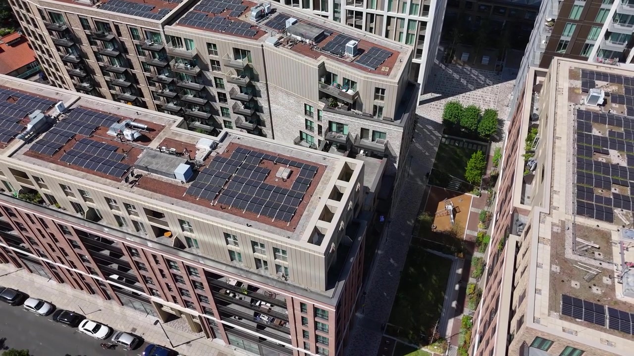 Fileiras de painéis solares cobrem os telhados de um novo empreendimento residencial, com varandas, pátios e um jardim paisagístico abaixo.