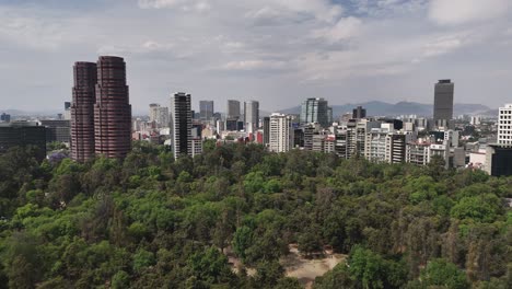 Dron-Elevándose-Sobre-El-Parque-Chapultepec,-Con-El-Barrio-De-Polanco-En-Cdmx-Al-Fondo