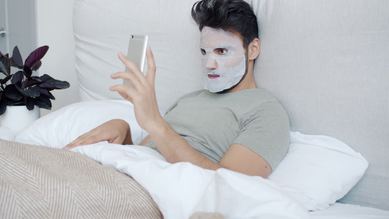 Man with face mask taking selfie on bed