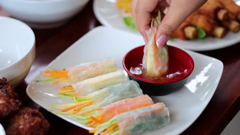 hand dipping a spring roll into sauce repeatedly