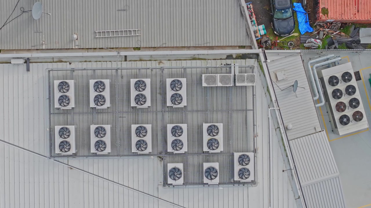 Riprese drone ad alta risoluzione mostrano il tetto di un data center industriale, ricco di unità di raffreddamento HVAC organizzate e ventilatori, offrendo una vista statica dall'alto in una luce diurna soffusa.