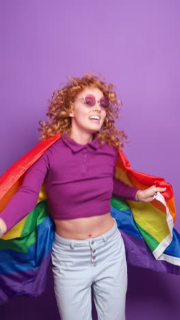 a woman celebrating with an lgbtq pride flag against a purple background