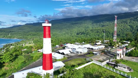 Red-and-white-lighthouse-on-the-Indonesian-border,-Papua-New-Guinea,-there-are-mountains-and-beautiful-blue-sky-clouds