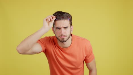 man adjusting glasses with a serious or questioning expression on a yellow background