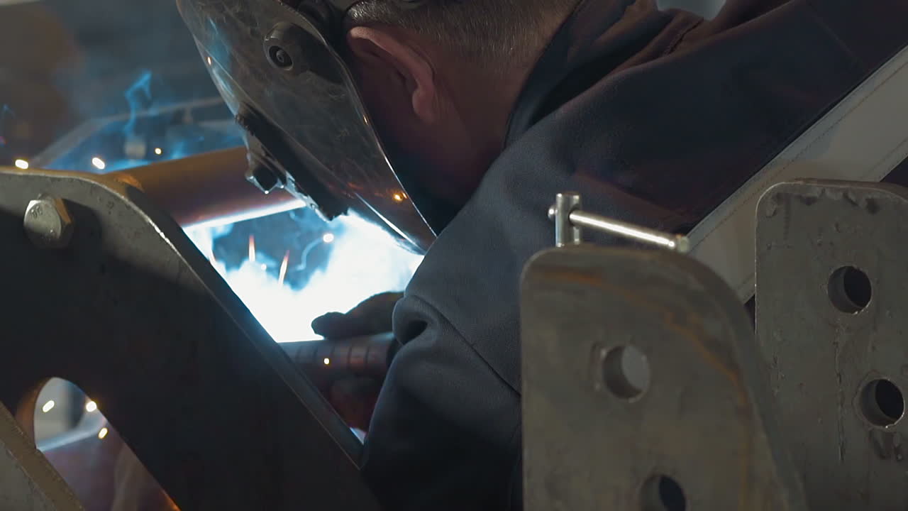 보호 마스크를 착용한 직원이 작업장에서 금속 프레임을 용접합니다.