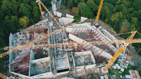 aerial view construction of a new building with high tower cranes in green area