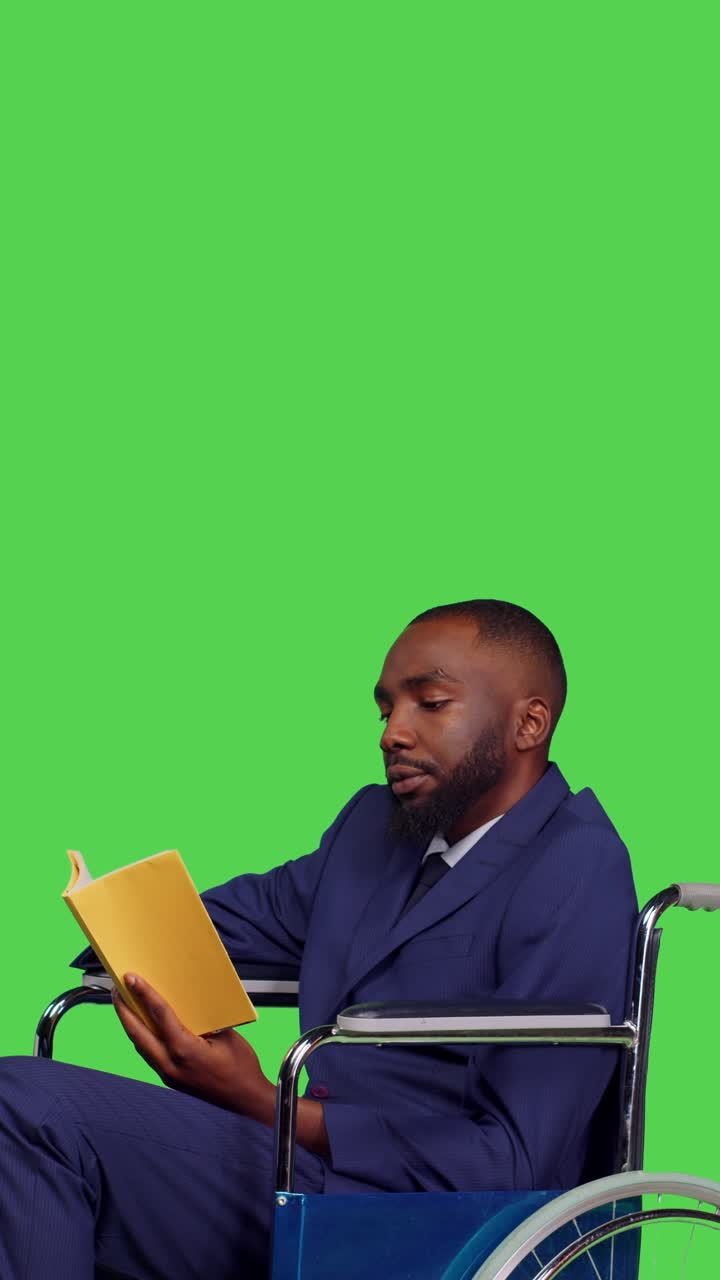 Vertical video: Side view of formal man wheelchair user reading novel story on book