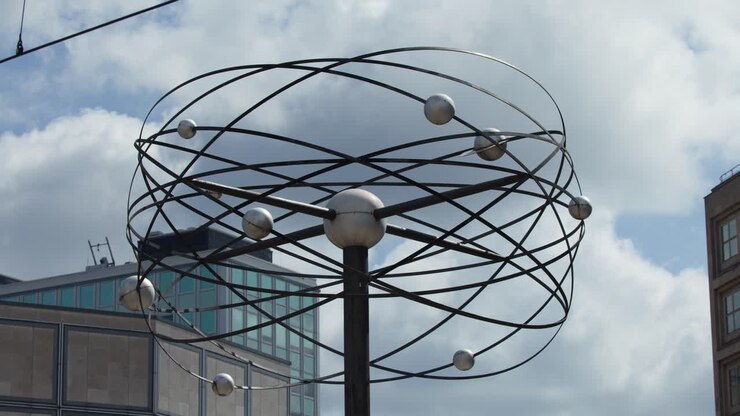 Una escultura de esfera metálica gira sobre un reloj emblemático con el paisaje urbano de Berlín de fondo, luz diurna, cámara estable, enfoque arquitectónico.