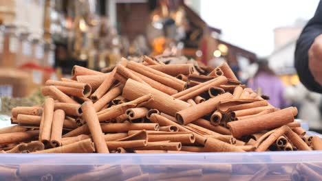 a hand reaches out to grab some cinnamon sticks at a market stall