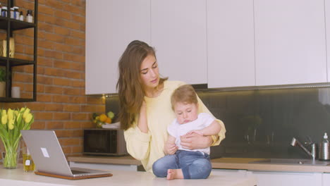 Woman-Holding-Her-Baby-On-The-Kitchen-Counter-While-Talking-On-The-Phone